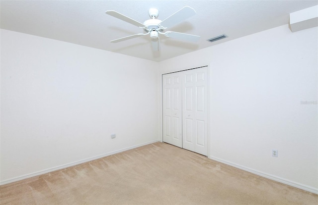 unfurnished bedroom featuring a closet, visible vents, a ceiling fan, light carpet, and baseboards