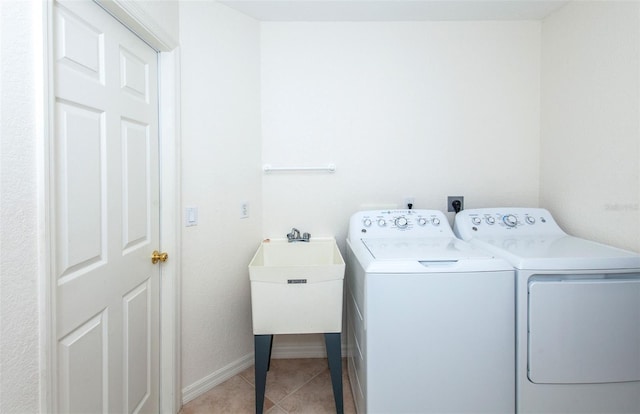 laundry area with light tile patterned floors, washing machine and dryer, a sink, laundry area, and baseboards