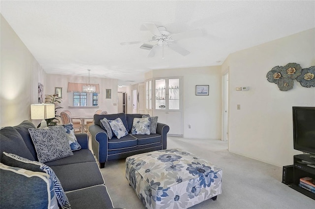 living area with a textured ceiling, light colored carpet, and ceiling fan with notable chandelier