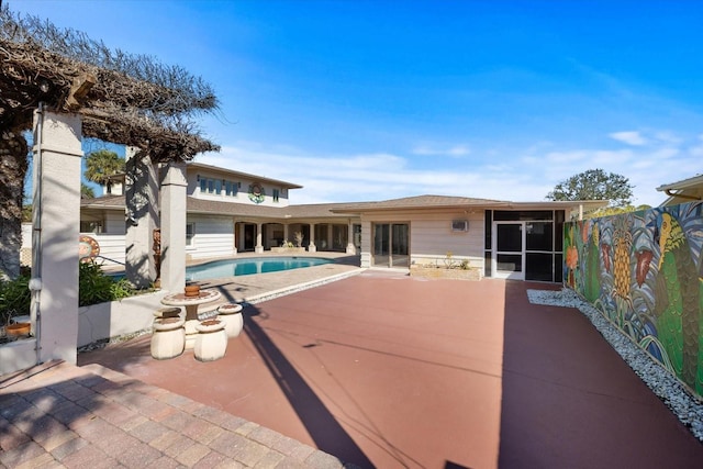 rear view of house featuring an outdoor pool, a patio, roof with shingles, and a sunroom