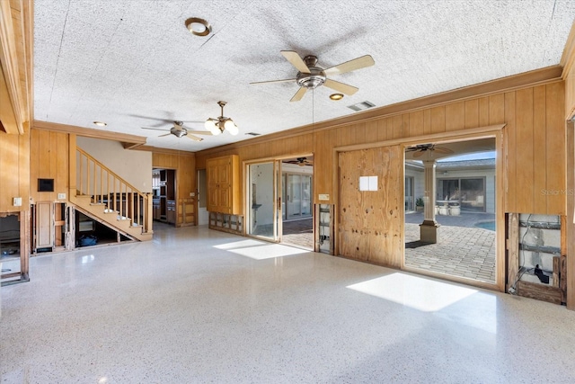 unfurnished living room with wood walls, stairs, speckled floor, and a ceiling fan