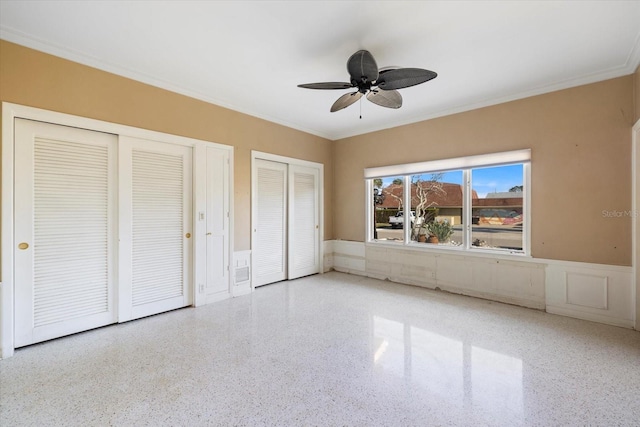 unfurnished bedroom featuring a wainscoted wall, speckled floor, multiple closets, and ornamental molding