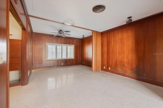 spare room featuring visible vents, light speckled floor, wood walls, and a ceiling fan