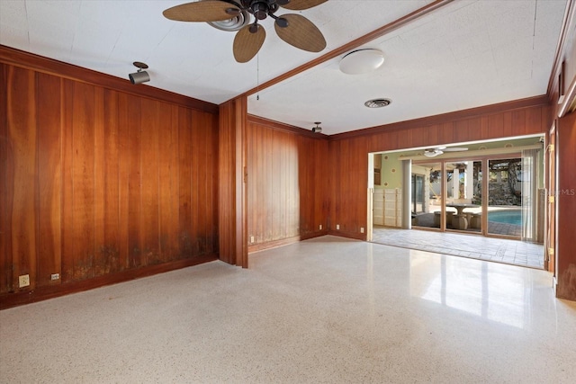 spare room featuring visible vents, baseboards, ceiling fan, wood walls, and speckled floor