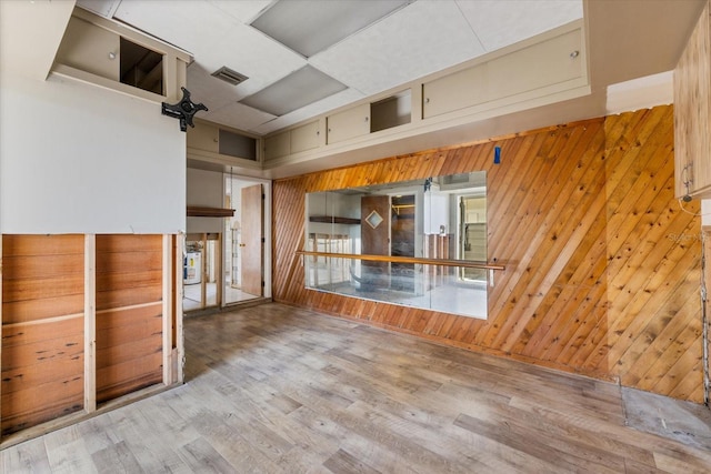 empty room with a high ceiling, wood finished floors, visible vents, and wood walls