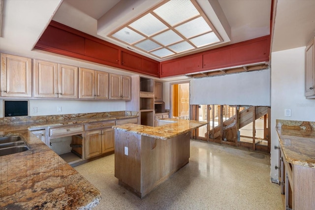 kitchen with a sink, light stone counters, light speckled floor, and a center island