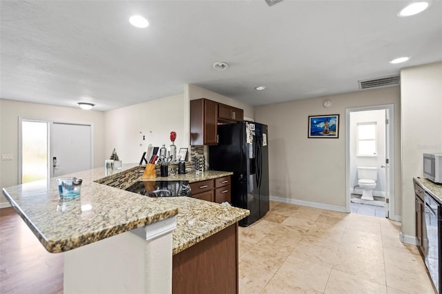 kitchen with a peninsula, visible vents, light stone countertops, black refrigerator with ice dispenser, and stainless steel microwave