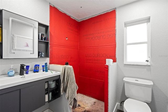 bathroom featuring toilet, a textured wall, concrete floors, and vanity
