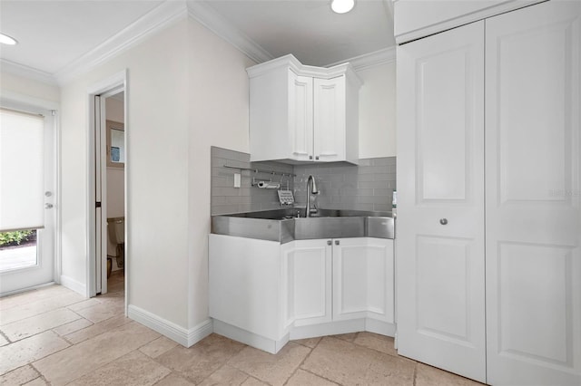 kitchen with white cabinetry, baseboards, tasteful backsplash, stone tile flooring, and crown molding