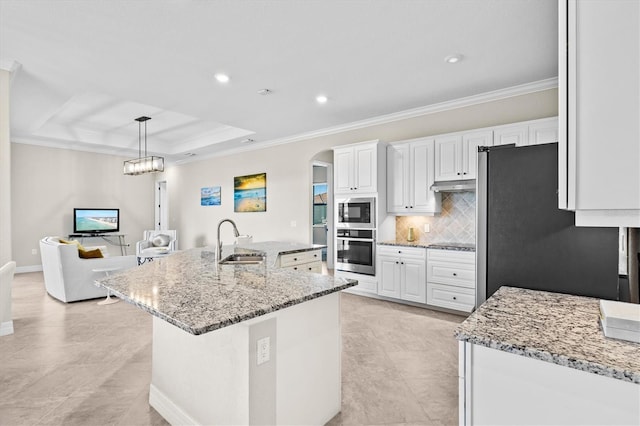 kitchen featuring arched walkways, a raised ceiling, appliances with stainless steel finishes, white cabinetry, and a sink