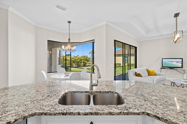 kitchen with light stone counters, visible vents, ornamental molding, a sink, and a chandelier