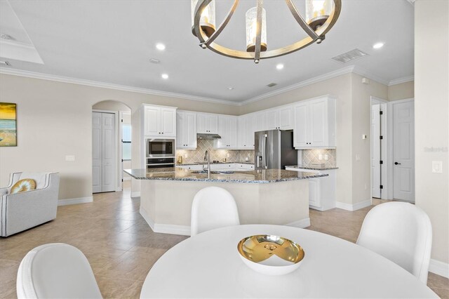 kitchen with tasteful backsplash, visible vents, a kitchen island with sink, stainless steel appliances, and under cabinet range hood