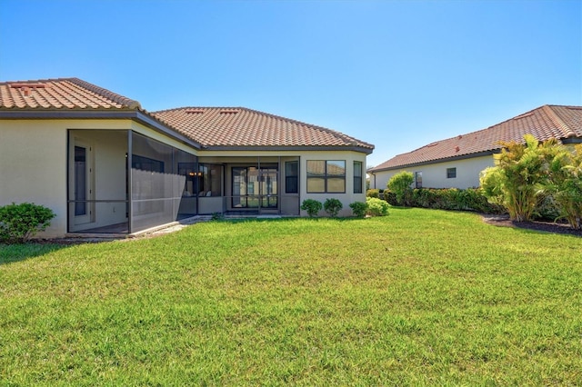 rear view of house with a sunroom, a tile roof, a yard, and stucco siding