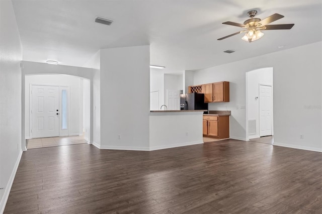 unfurnished living room with visible vents, arched walkways, dark wood-type flooring, and a ceiling fan