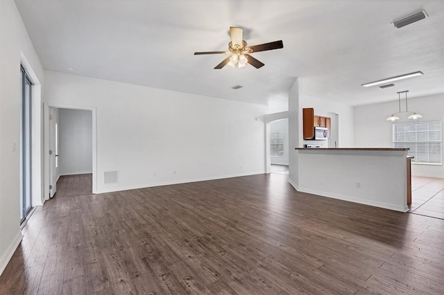 unfurnished living room with dark wood-style floors, visible vents, baseboards, and ceiling fan