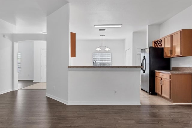 kitchen featuring decorative light fixtures, wood finished floors, arched walkways, and black fridge