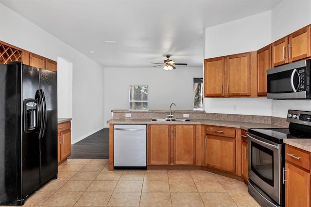 kitchen featuring light tile patterned floors, a peninsula, brown cabinetry, stainless steel appliances, and a sink