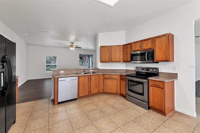 kitchen featuring light tile patterned floors, brown cabinets, appliances with stainless steel finishes, a peninsula, and a sink