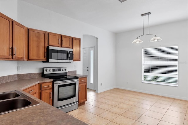 kitchen featuring baseboards, hanging light fixtures, brown cabinets, appliances with stainless steel finishes, and arched walkways