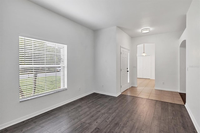 empty room with arched walkways, dark wood-style floors, and baseboards