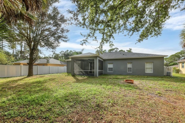 back of house featuring a yard, fence, a sunroom, and a fire pit