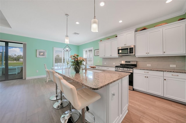 kitchen with visible vents, stainless steel appliances, light wood-type flooring, white cabinetry, and backsplash