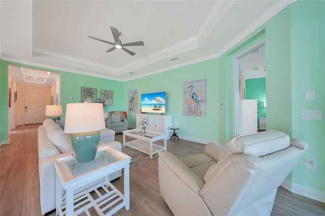 living area featuring ornamental molding, a tray ceiling, visible vents, and wood finished floors