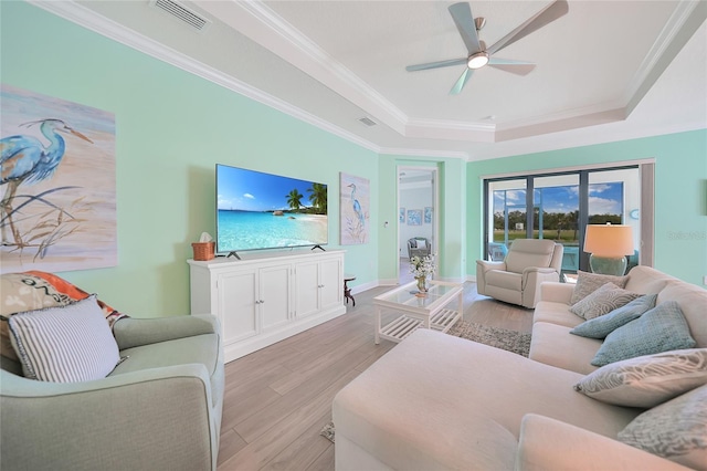 living area with a ceiling fan, visible vents, light wood finished floors, a raised ceiling, and crown molding