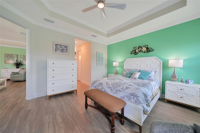 bedroom featuring ornamental molding, a raised ceiling, visible vents, and wood finished floors