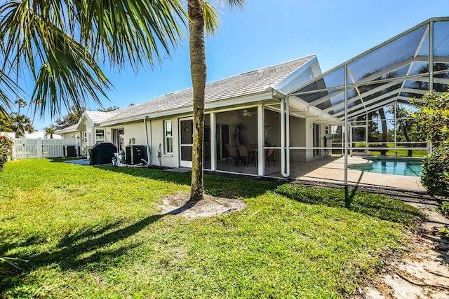 rear view of property featuring fence, stucco siding, a lawn, glass enclosure, and an outdoor pool