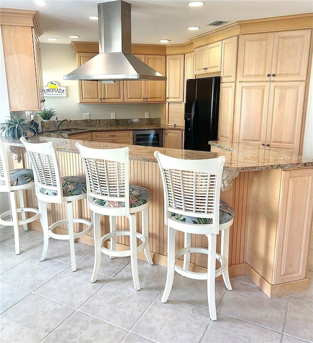 kitchen featuring visible vents, a kitchen bar, black fridge, a peninsula, and island exhaust hood