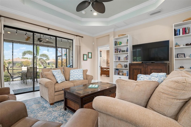 tiled living room with ceiling fan, visible vents, built in features, ornamental molding, and a raised ceiling