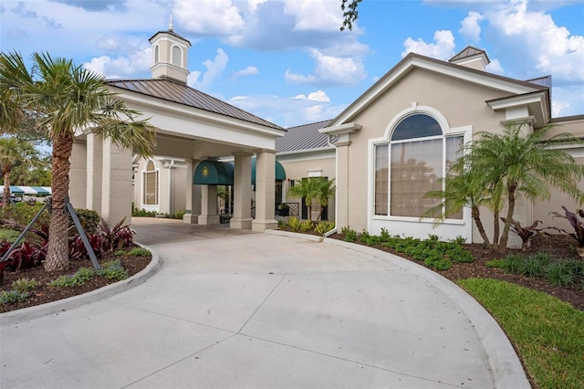 entrance to property with a standing seam roof, driveway, metal roof, and stucco siding