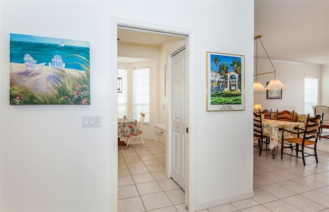 hallway with baseboards, ornamental molding, and light tile patterned flooring