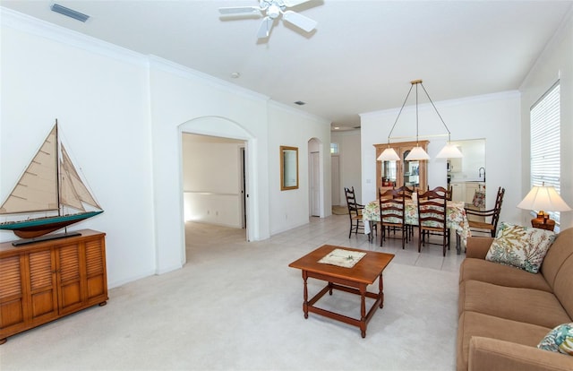 living area featuring arched walkways, light colored carpet, visible vents, ornamental molding, and ceiling fan