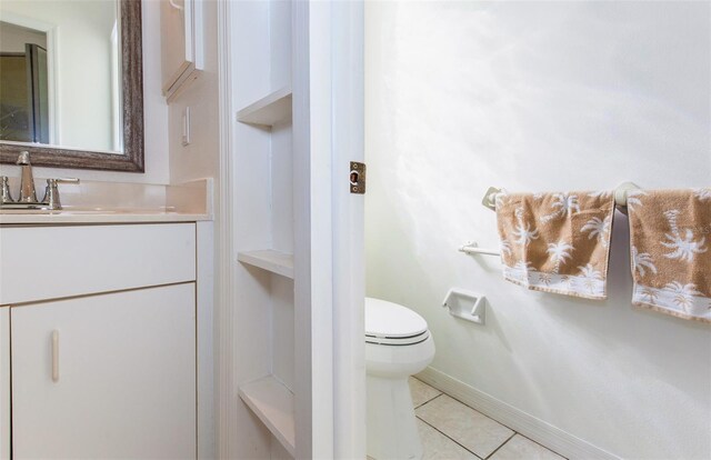 half bathroom with baseboards, vanity, toilet, and tile patterned floors