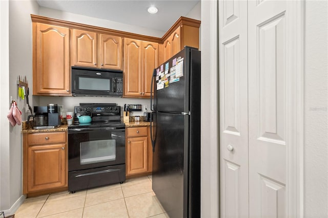 kitchen featuring black appliances, stone counters, light tile patterned flooring, and brown cabinets