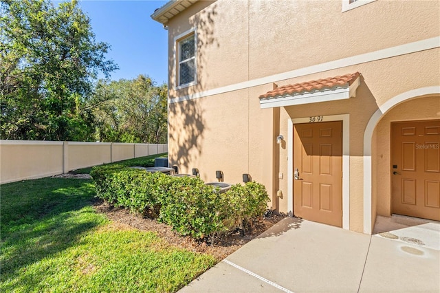 entrance to property with a yard, a tile roof, fence, and stucco siding
