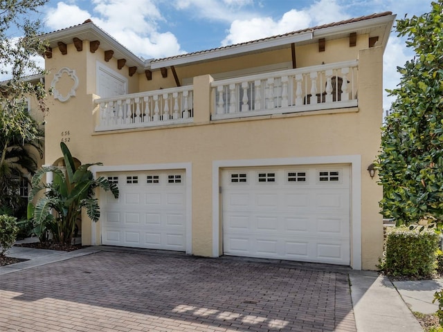 view of front facade with decorative driveway, an attached garage, a balcony, and stucco siding