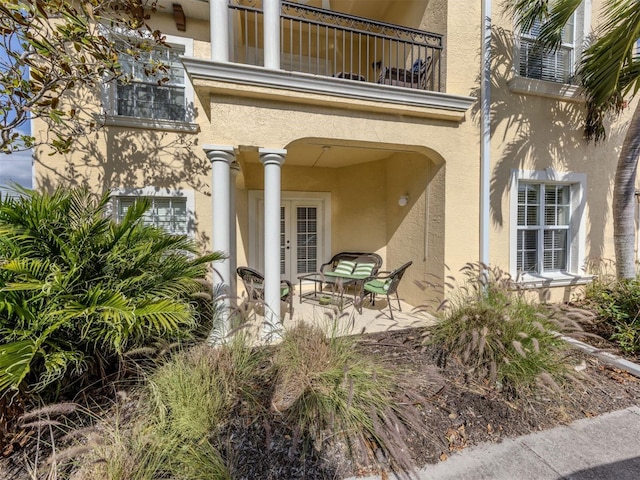 entrance to property with french doors, a patio area, a balcony, and stucco siding