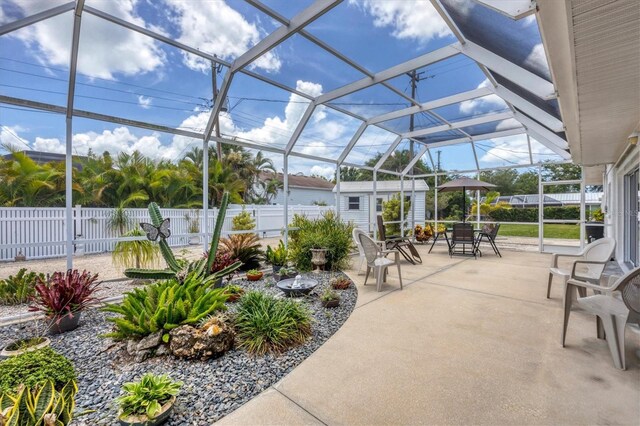 view of patio featuring glass enclosure, an outbuilding, fence private yard, a shed, and outdoor dining space