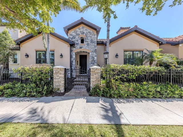 view of front of house featuring stucco siding, stone siding, a fenced front yard, and a tiled roof