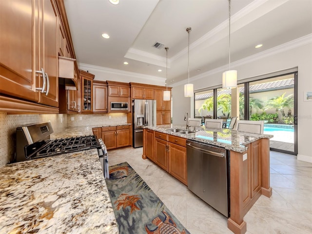 kitchen with visible vents, brown cabinetry, stainless steel appliances, a raised ceiling, and a kitchen island with sink