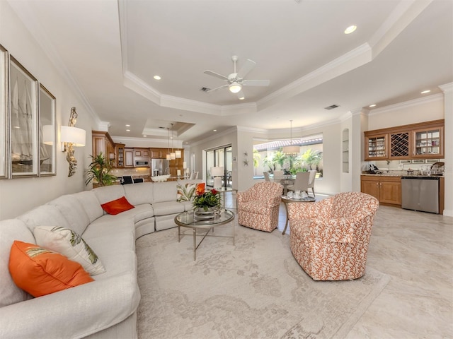 living room with ornamental molding, recessed lighting, wet bar, a raised ceiling, and ceiling fan