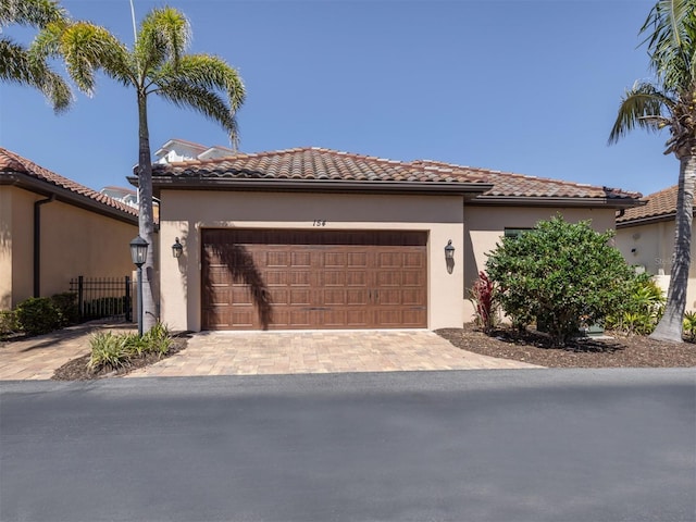 mediterranean / spanish house with fence, a tiled roof, stucco siding, decorative driveway, and an attached garage