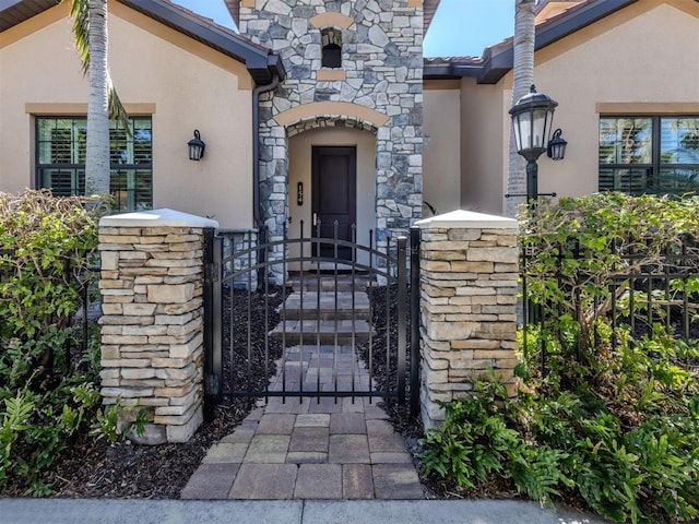 property entrance with a tiled roof, stucco siding, stone siding, and a gate