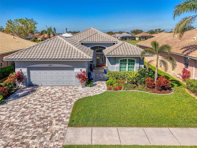 mediterranean / spanish-style home featuring a garage, a tile roof, french doors, decorative driveway, and a front yard