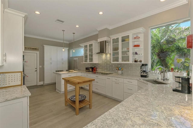 kitchen featuring visible vents, black electric cooktop, wall chimney range hood, white cabinetry, and a sink