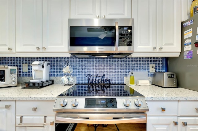 kitchen with tasteful backsplash, white cabinets, stainless steel appliances, and light stone counters