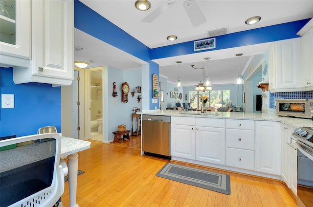 kitchen featuring visible vents, a peninsula, a sink, stainless steel appliances, and white cabinets